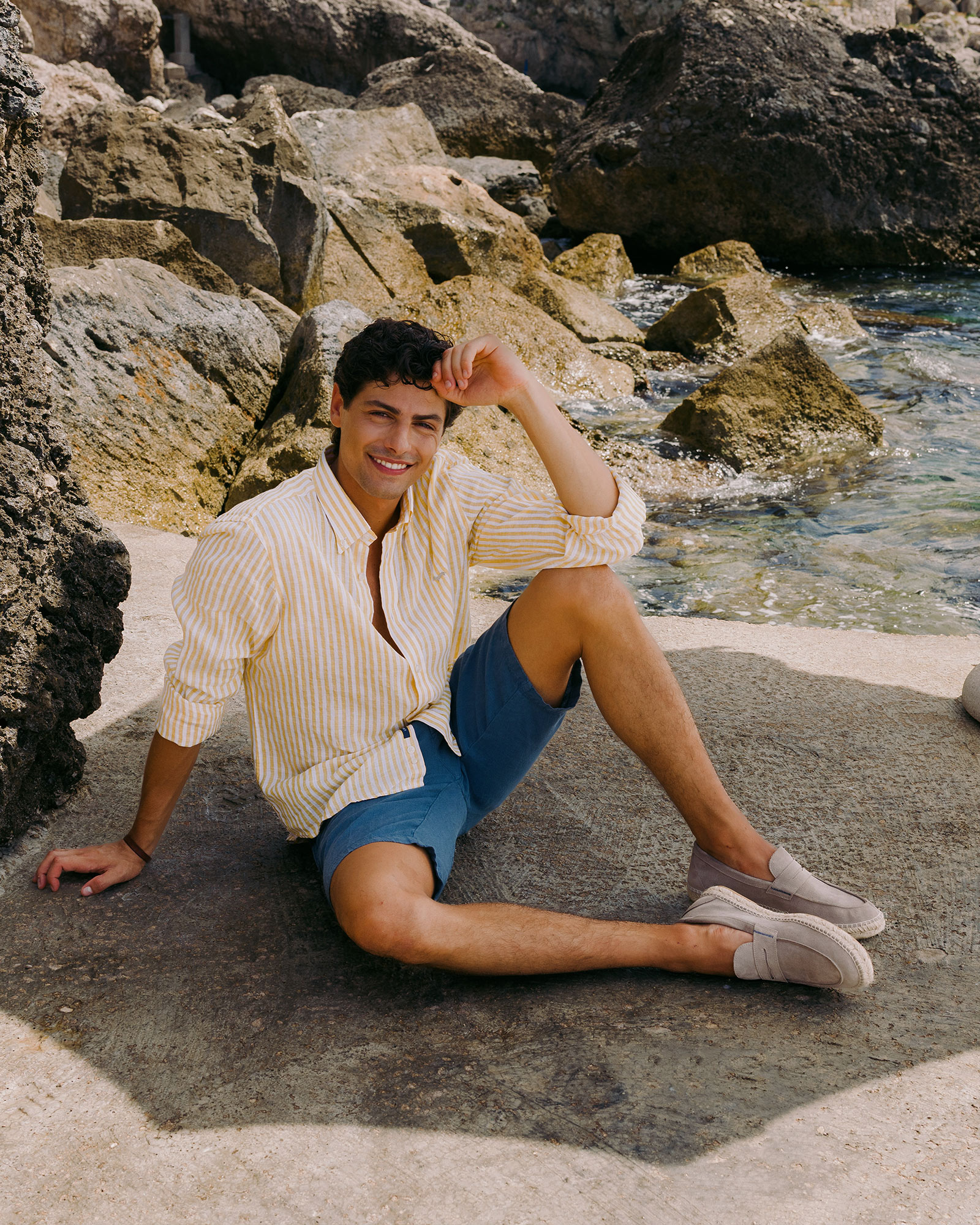 Man sitting on rocks in yellow striped shirt and shorts